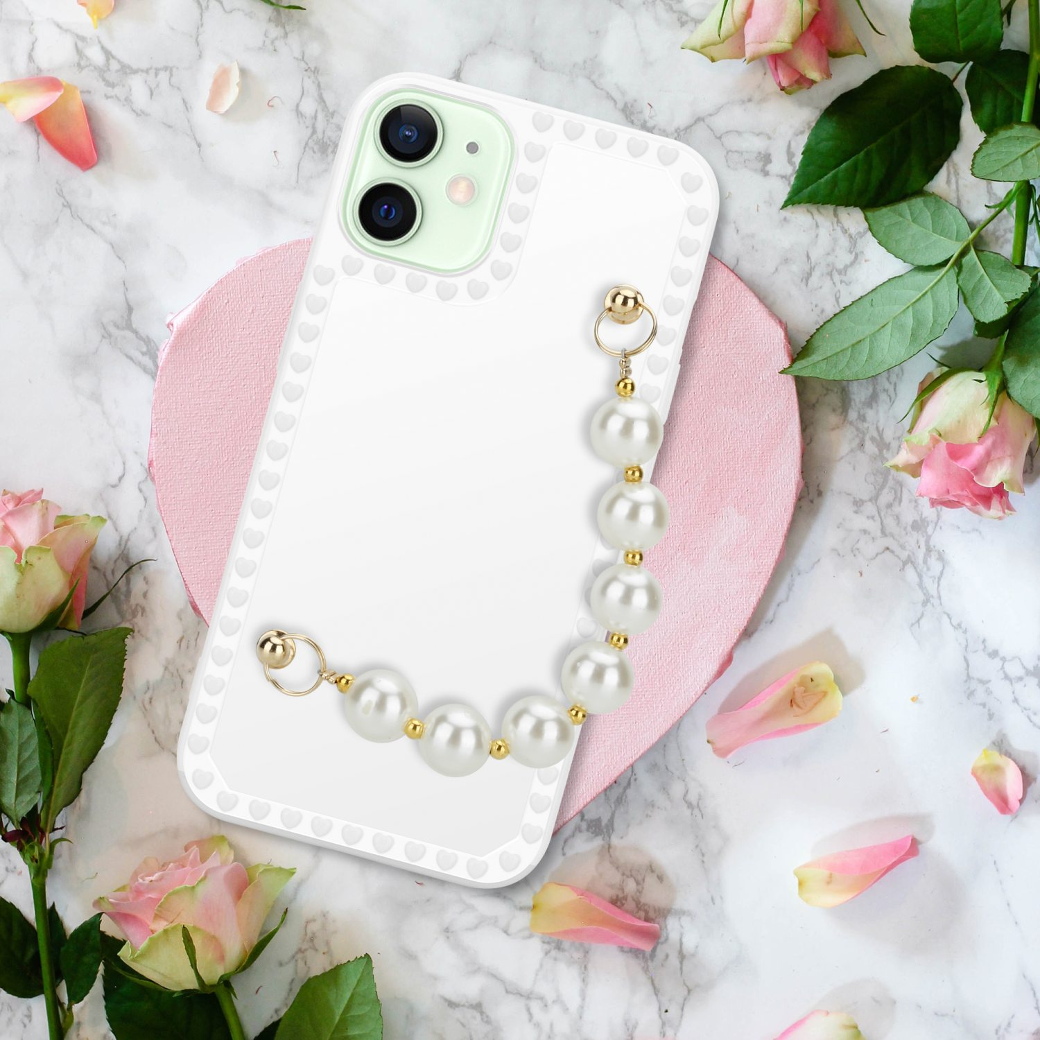 Eine weiße Handyhülle mit Perlband liegt auf Marmor mit rosa Rosen und Blütenblättern.