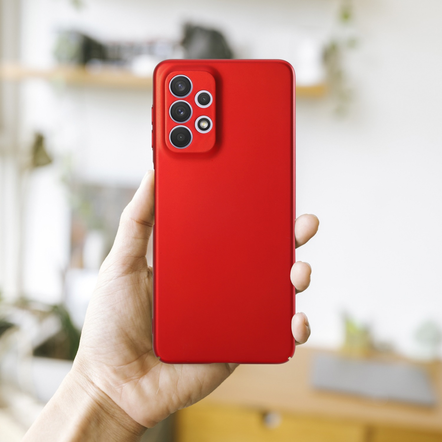 Hand hält eine rote Handyhülle mit Kameraschutz. Die Hülle ist schlicht rot, mit strukturierter Oberfläche. Weißer Hintergrund.