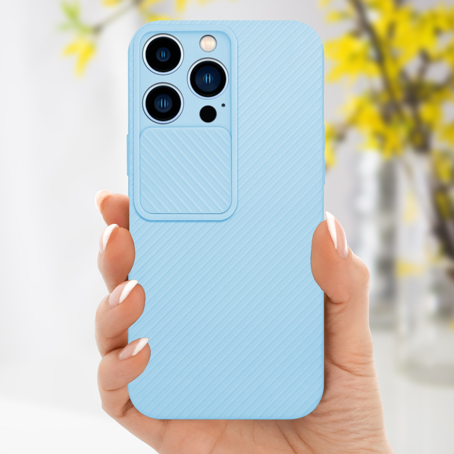 Mano che tiene una custodia per telefono azzurra con una copertura per la fotocamera. Fiori gialli sullo sfondo.