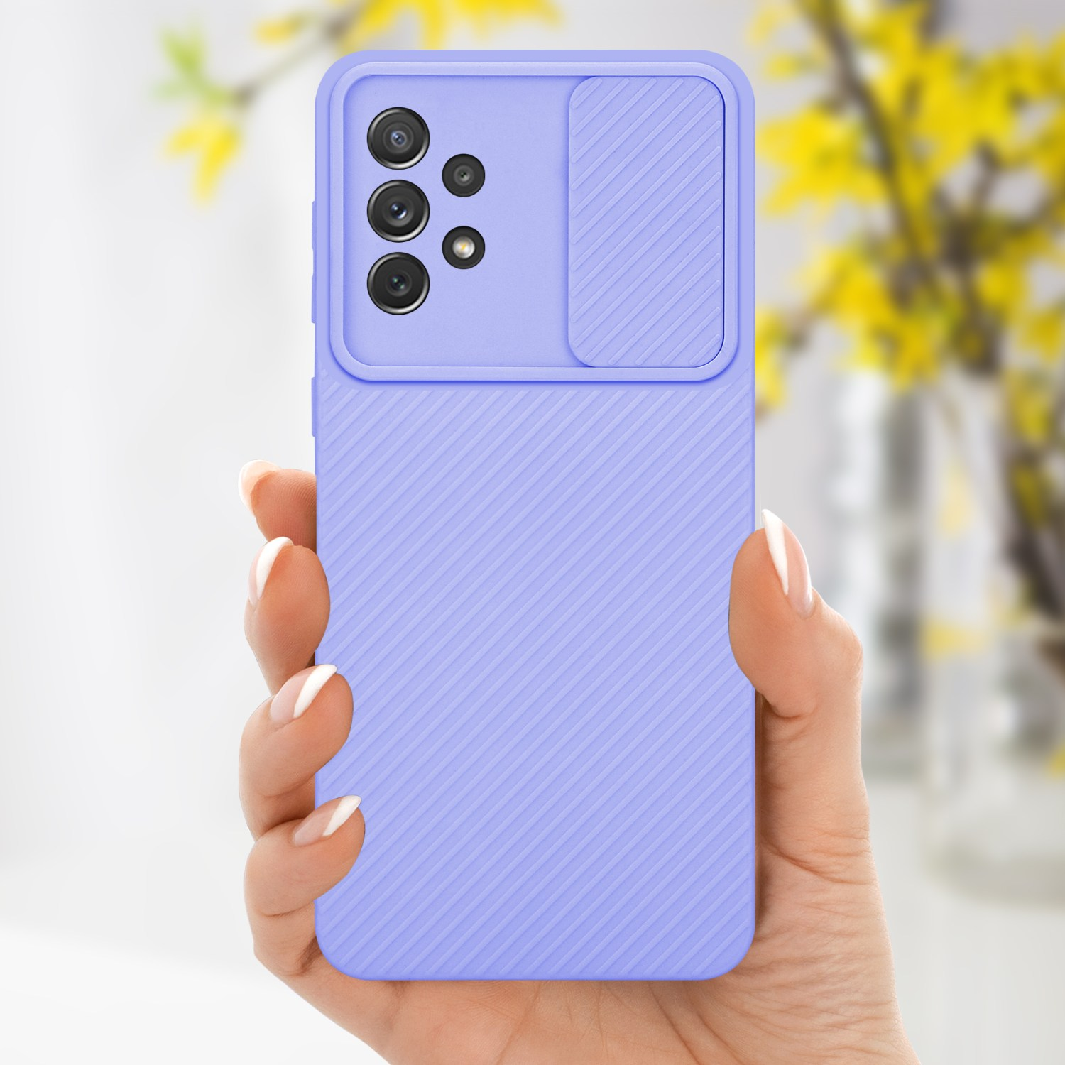 Hand hält eine lila Handyhülle mit Kameraabdeckung. Hintergrund zeigt verschwommene Blumen.