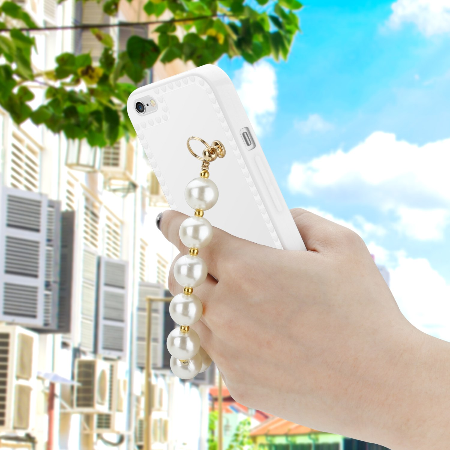 Ein weißes Telefon mit Perlenband wird von einer Hand gehalten. Der Hintergrund ist eine Stadtstraße und Himmel.