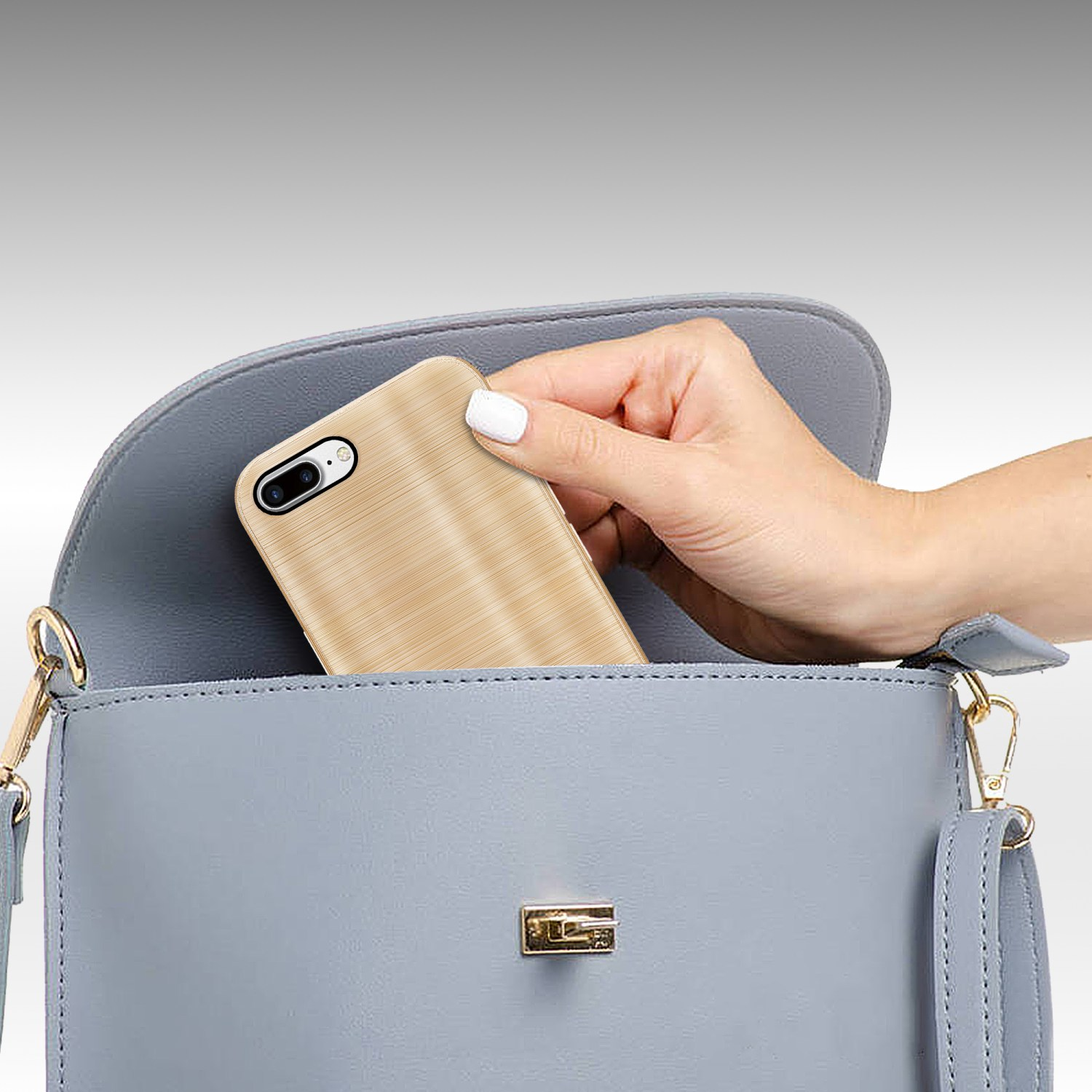 Hand legt ein goldenes Telefon in eine blaue Handtasche. Die Handtasche ist offen.
