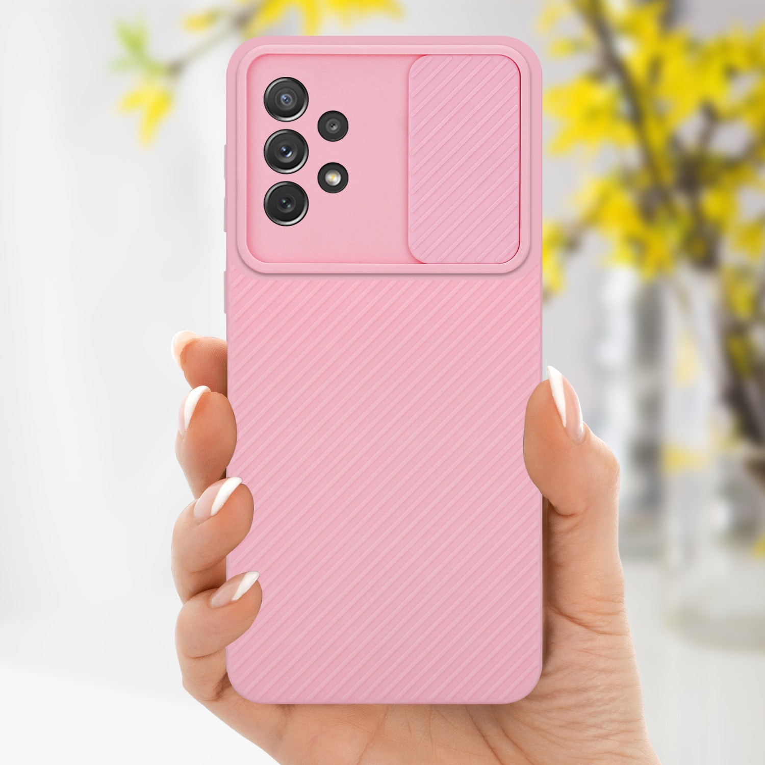 Hand hält eine rosa Handyhülle mit Kameraschieber. Gelbe Blumen sind im unscharfen Hintergrund.