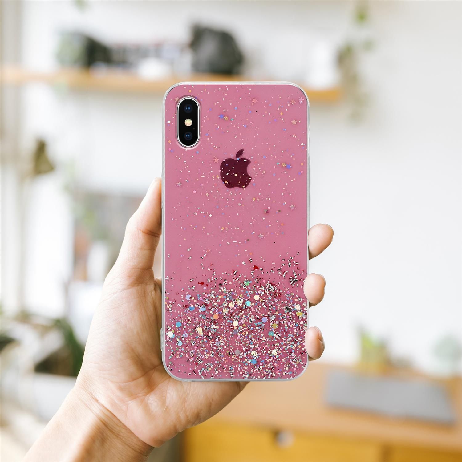 Eine Hand, die eine rosa Handyhülle mit Glitzer und Apple-Logo hält, vor verschwommenem Hintergrund.