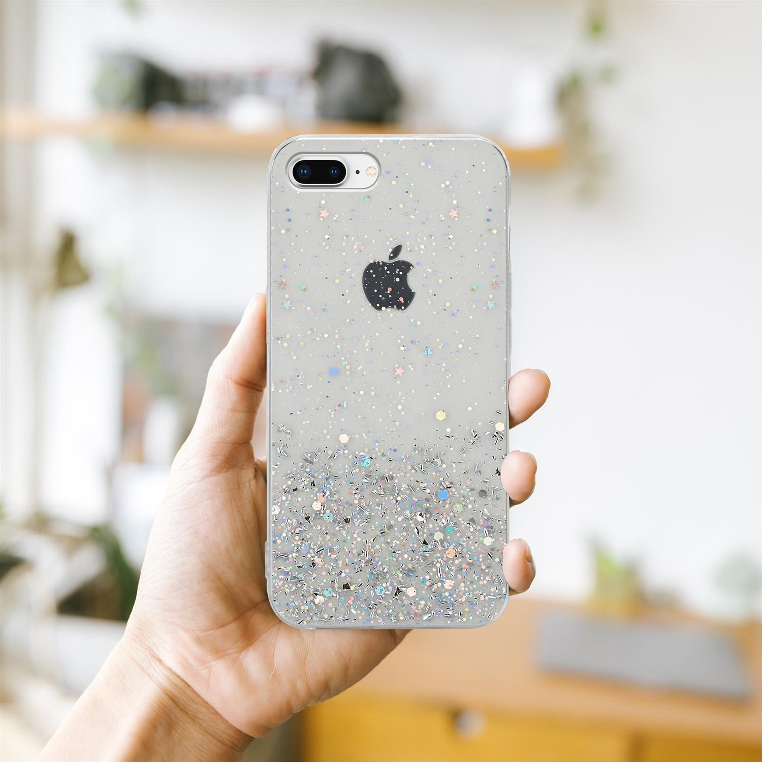 Hand hält ein Telefon in einer durchsichtigen Glitzerhülle. Apple-Logo auf der Rückseite.