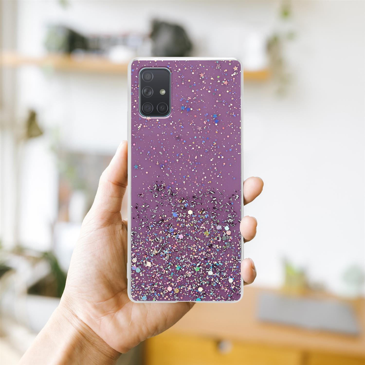 Hand hält eine Handyhülle. Lila Glitzerdesign auf der Rückseite. Verschwommener Hintergrund.