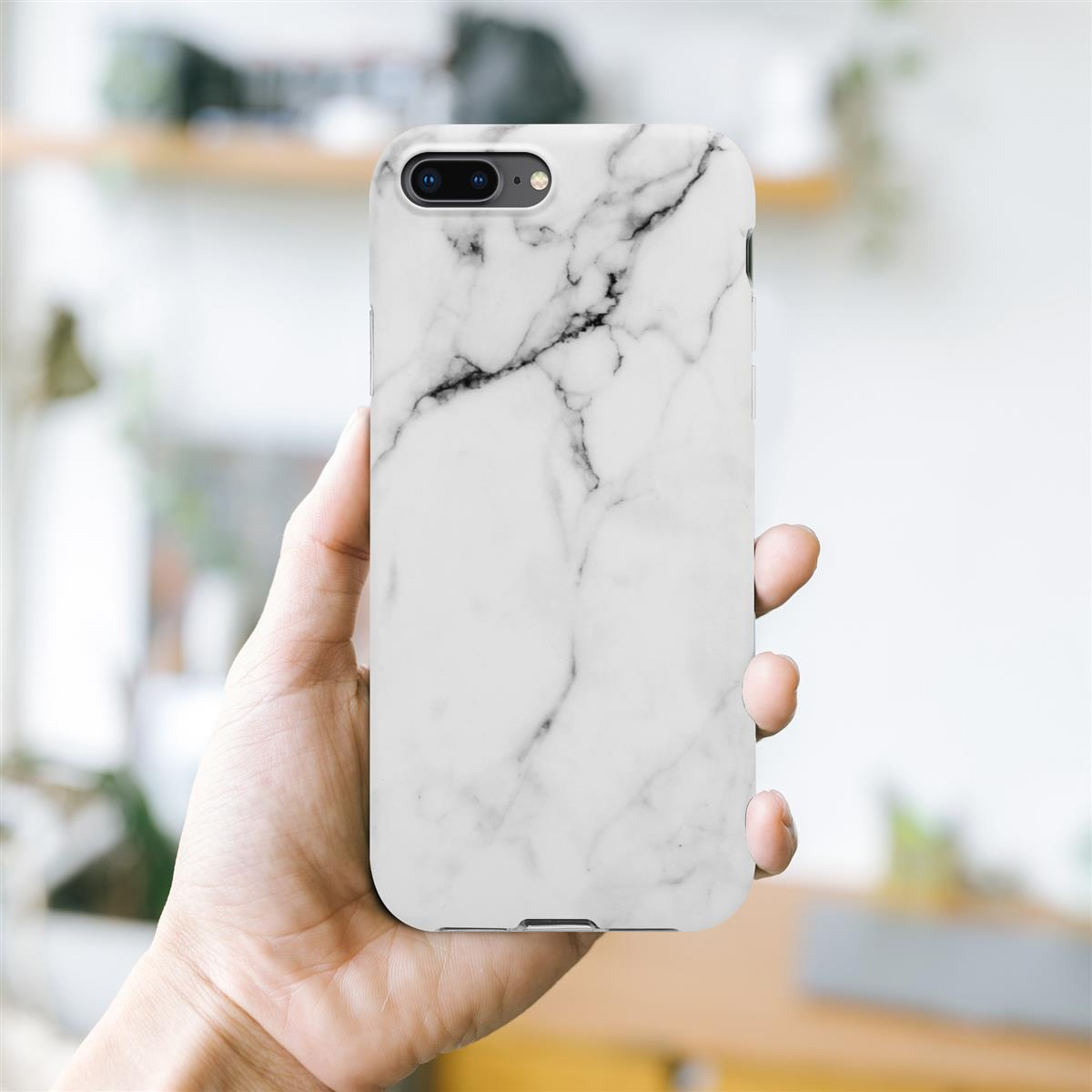 Eine Person hält eine weiße Handyhülle mit schwarzem Marmordesign. Hintergrund ist ein heller Raum und Regal.