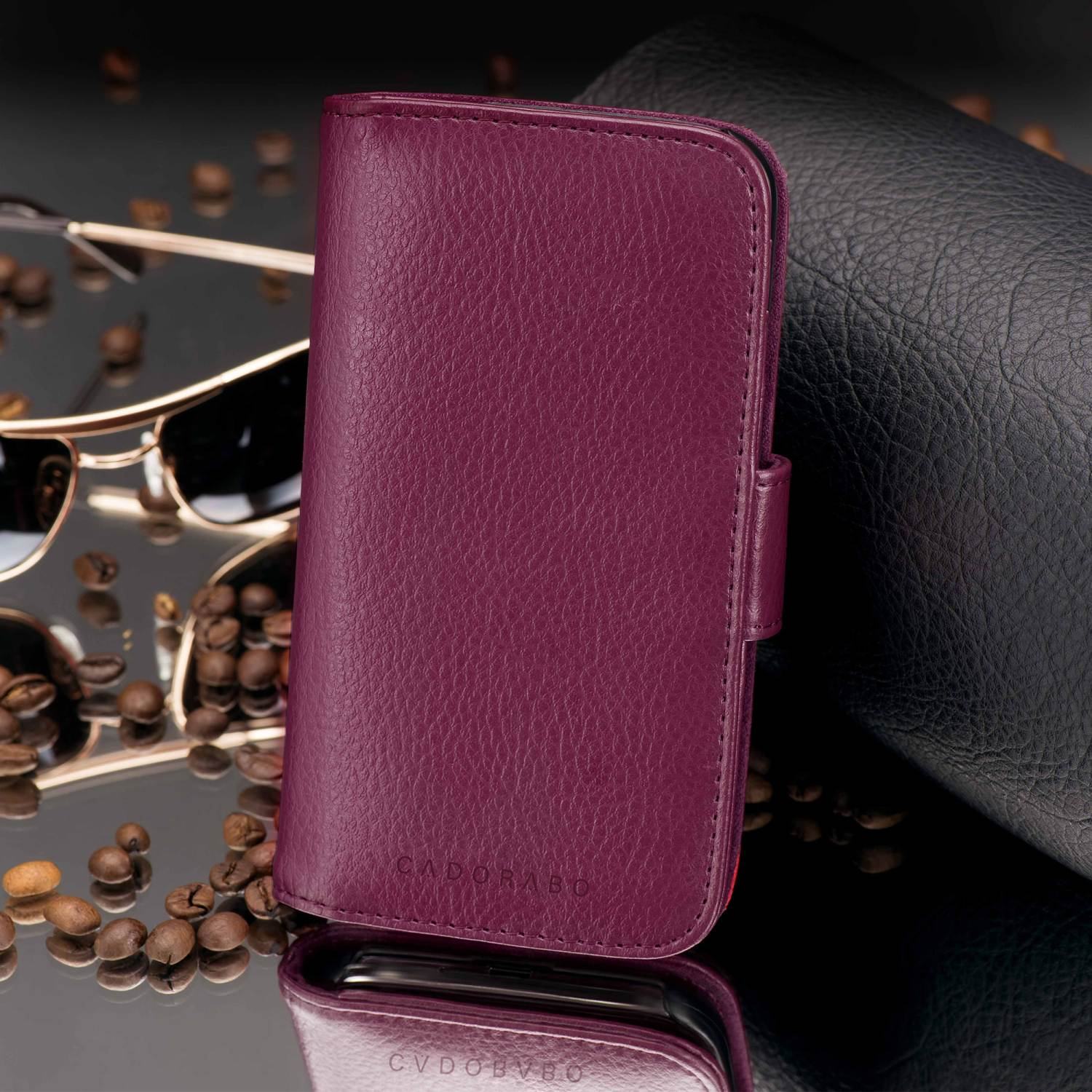 Burgunderfarbenes Handy-Case mit Magnetverschluss, Kaffeebohnen und Sonnenbrille spiegeln sich auf schwarzer Oberfläche.