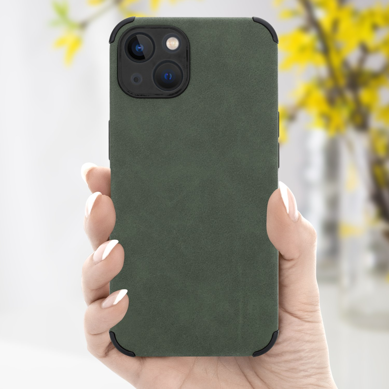 Hand hält eine grüne Handyhülle mit schwarzer Kamera, mit verschwommenem Hintergrund von Blumen.