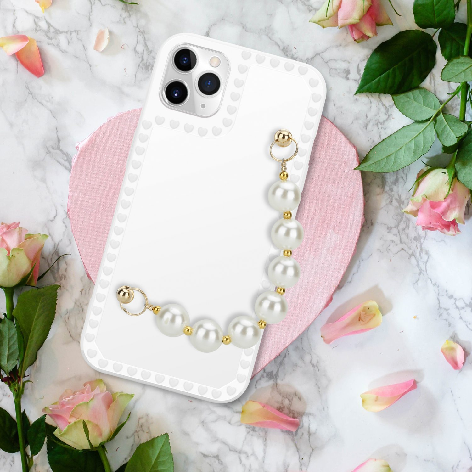 Weißes Handycase mit Perlenarmband, Rosen und Blütenblättern auf Marmoroberfläche.