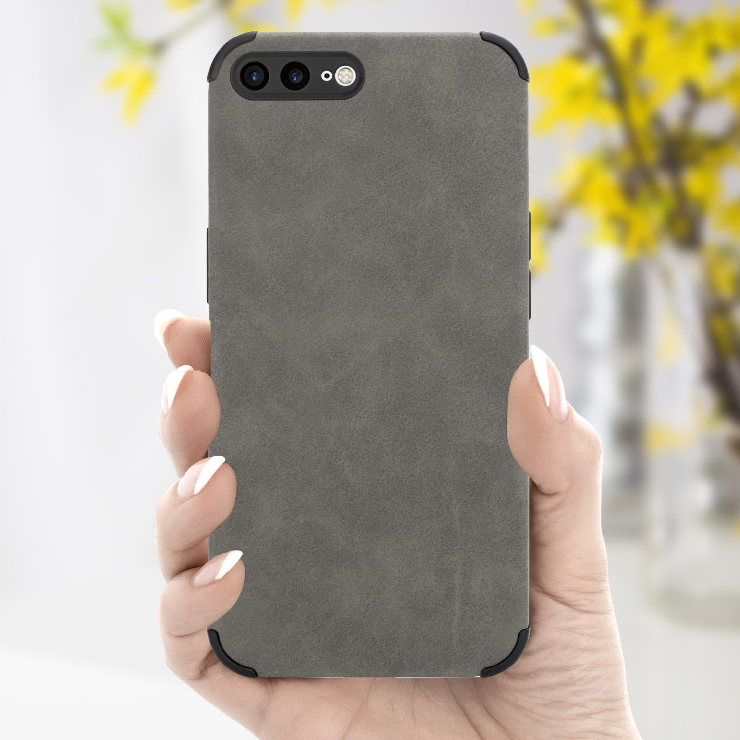 Hand, die Telefon in grauer Hülle hält. Hintergrund hat gelbe Blumen. Drei Kameras sind sichtbar.