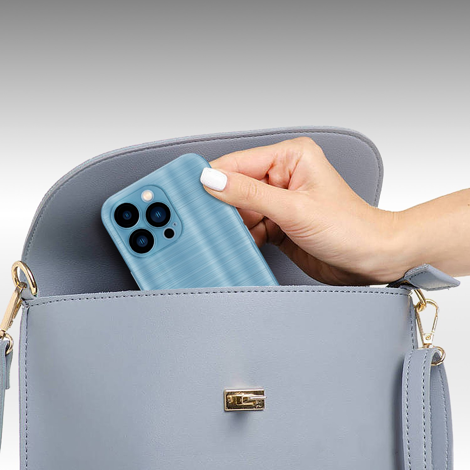 Mano metiendo una funda azul para teléfono con aspecto de metal cepillado en un bolso gris.