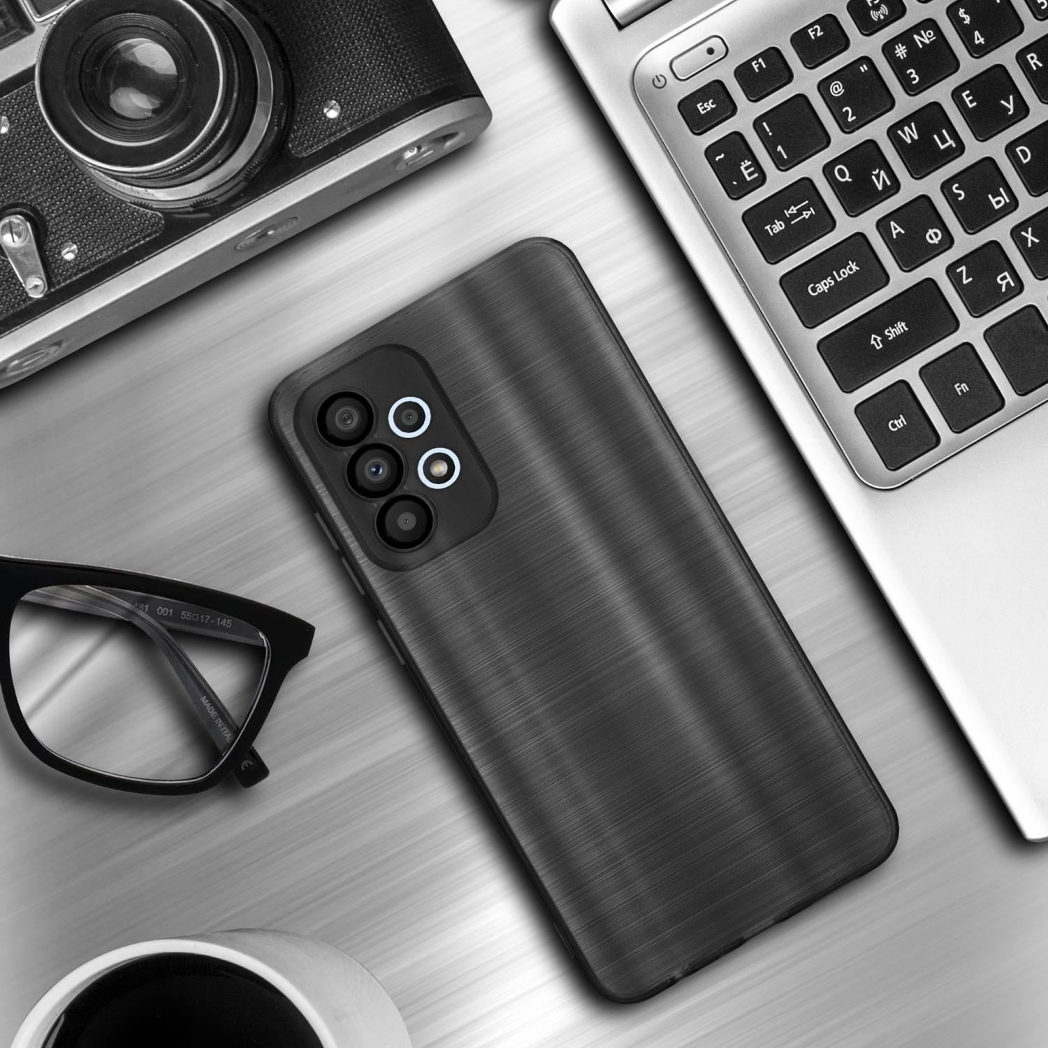 Eine Handyhülle liegt auf einem Schreibtisch neben einem Laptop, einer Kamera und einer Brille. Die Hülle ist schwarz mit gebürstetem Metalldesign.