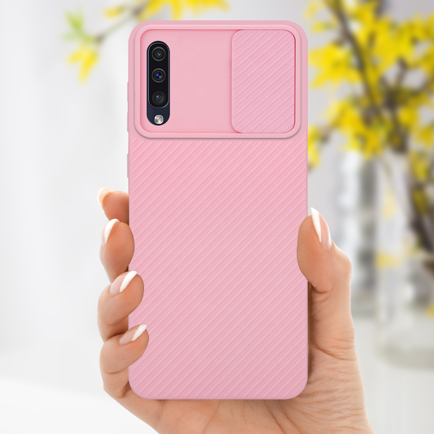 Hand hält eine rosa Handyhülle. Ein Strauß Blumen ist im Hintergrund zu sehen.