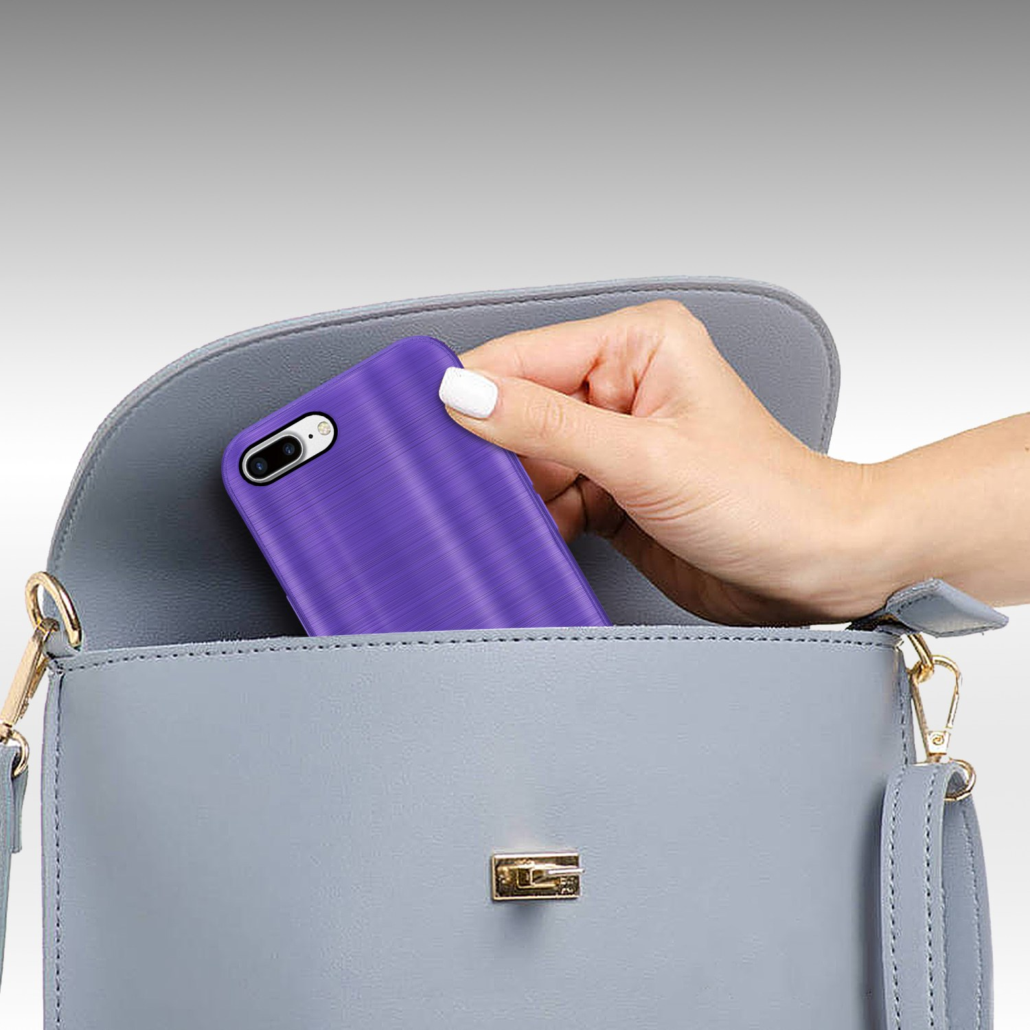 Eine Hand legt ein lila Telefon in eine hellgraue Handtasche. Das Telefon hat gebürstete Metalloptik.