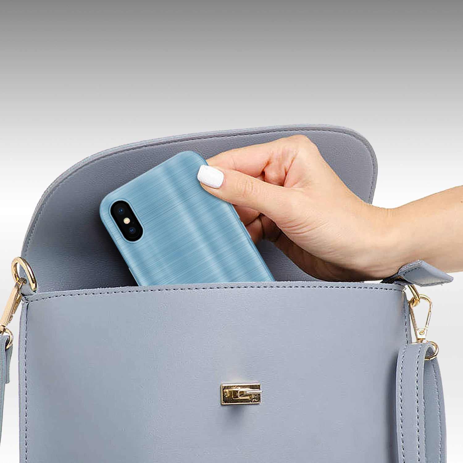 Eine Hand, die ein blaues Telefon mit strukturierter Hülle in eine graue Handtasche legt, auf grauem Hintergrund.