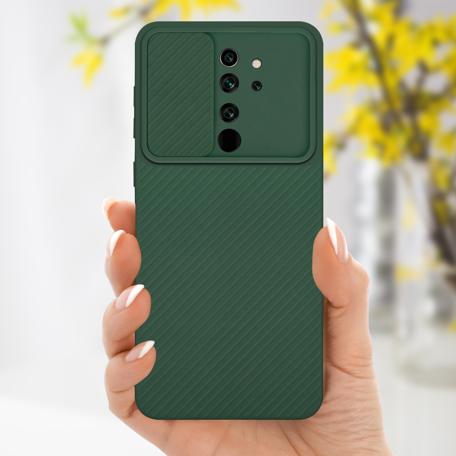 Custodia per telefono verde scuro, mano che la tiene. Fiori gialli sfocati sullo sfondo.