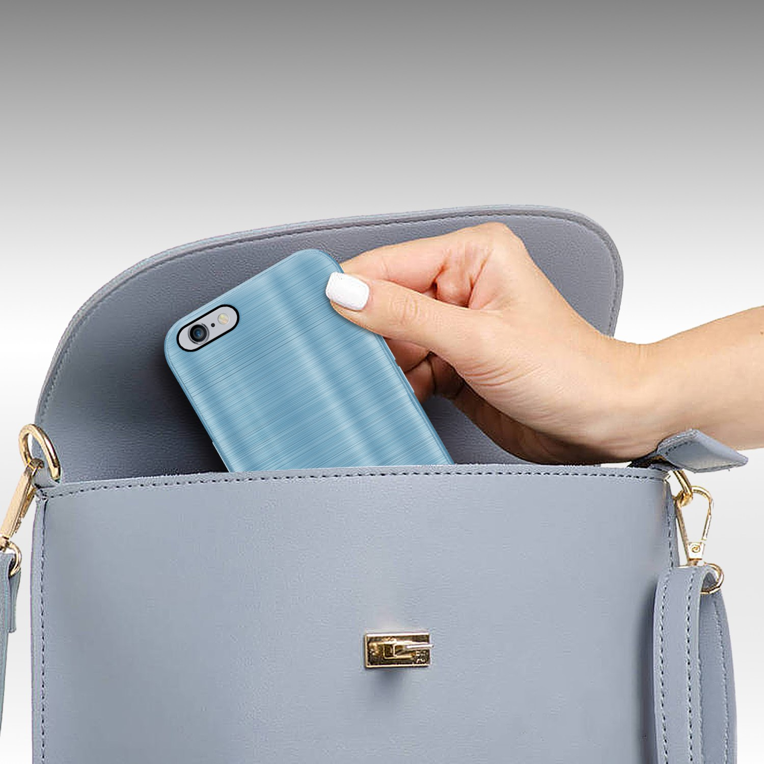 Eine Hand legt eine blaue Handyhülle in eine graue Handtasche, auf grauem Hintergrund.