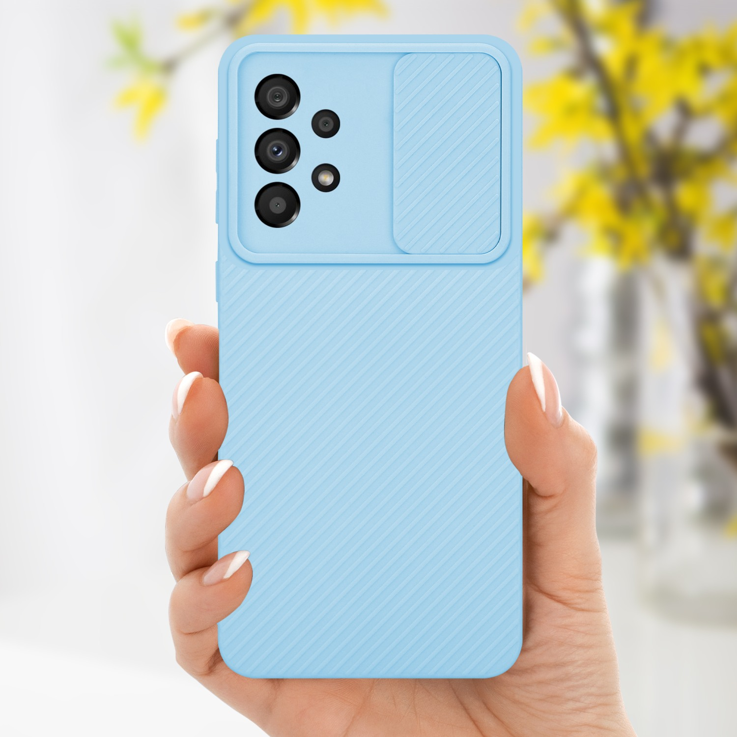 Mano che tiene una custodia per telefono azzurra con copertura per fotocamera. Fiori gialli sullo sfondo.