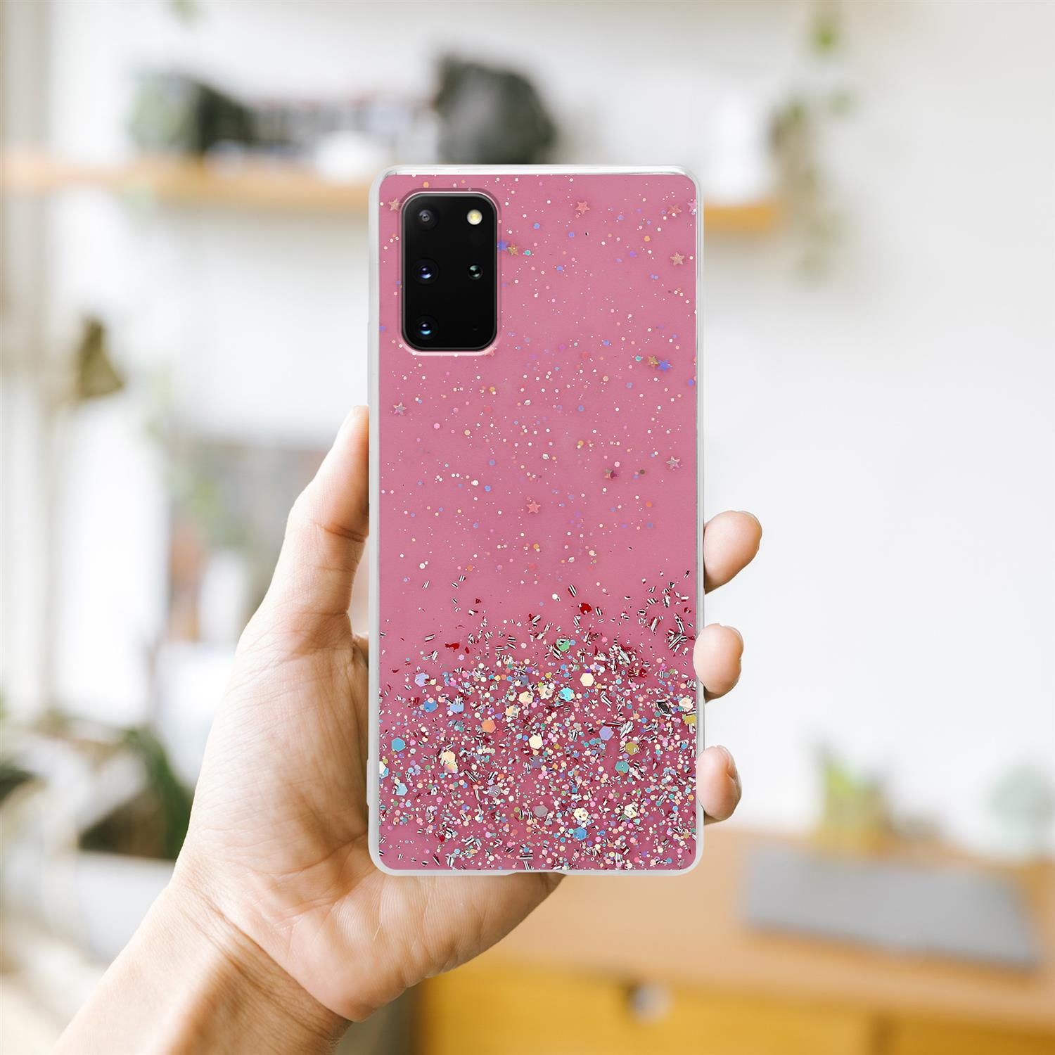 Eine Hand, die eine pinkfarbene Handyhülle mit Glitzer hält. Hintergrund: ein verschwommener Raum.