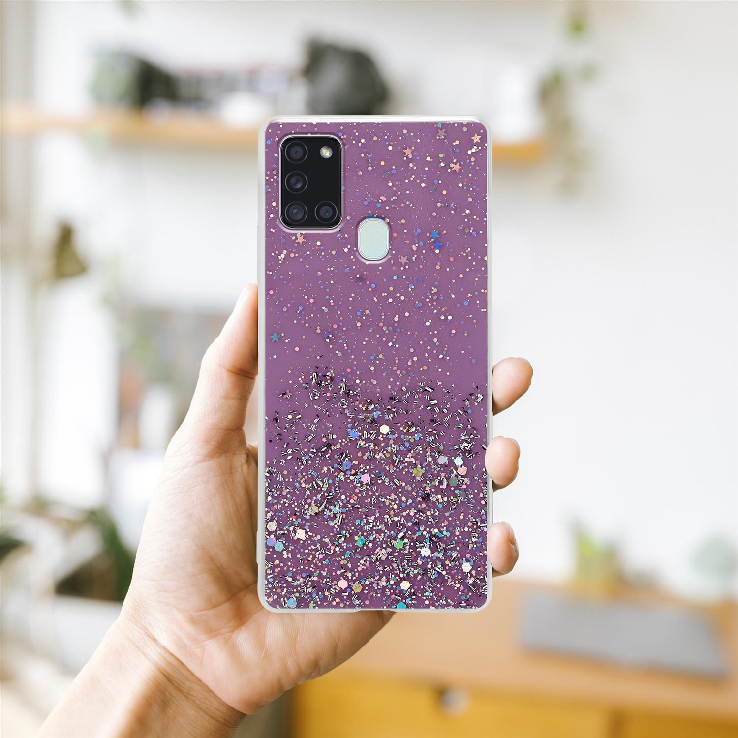 Hand hält Handyhülle mit Glitzer auf unscharfem Hintergrund.