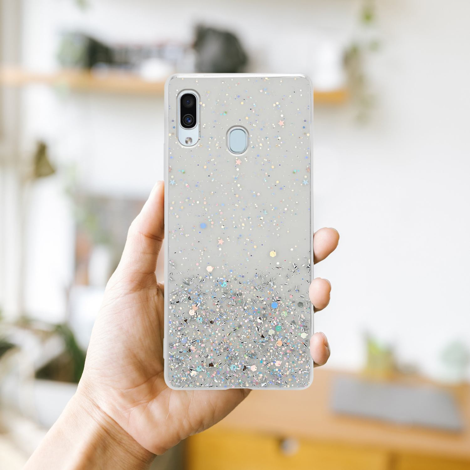 Eine Hand, die eine mit Glitzer bedeckte Handyhülle hält, mit unscharfem Hintergrund.
