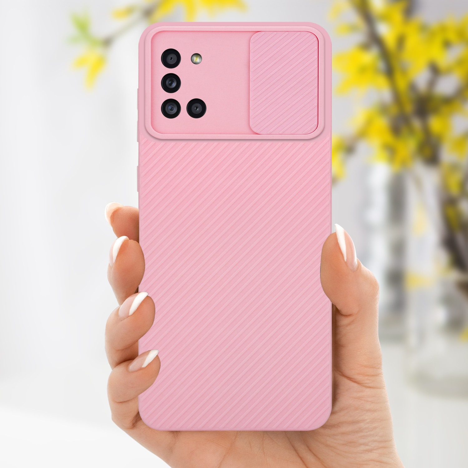 Eine Hand hält eine rosa Handyhülle mit Kameraabdeckung vor einem verschwommenen Blumenhintergrund.