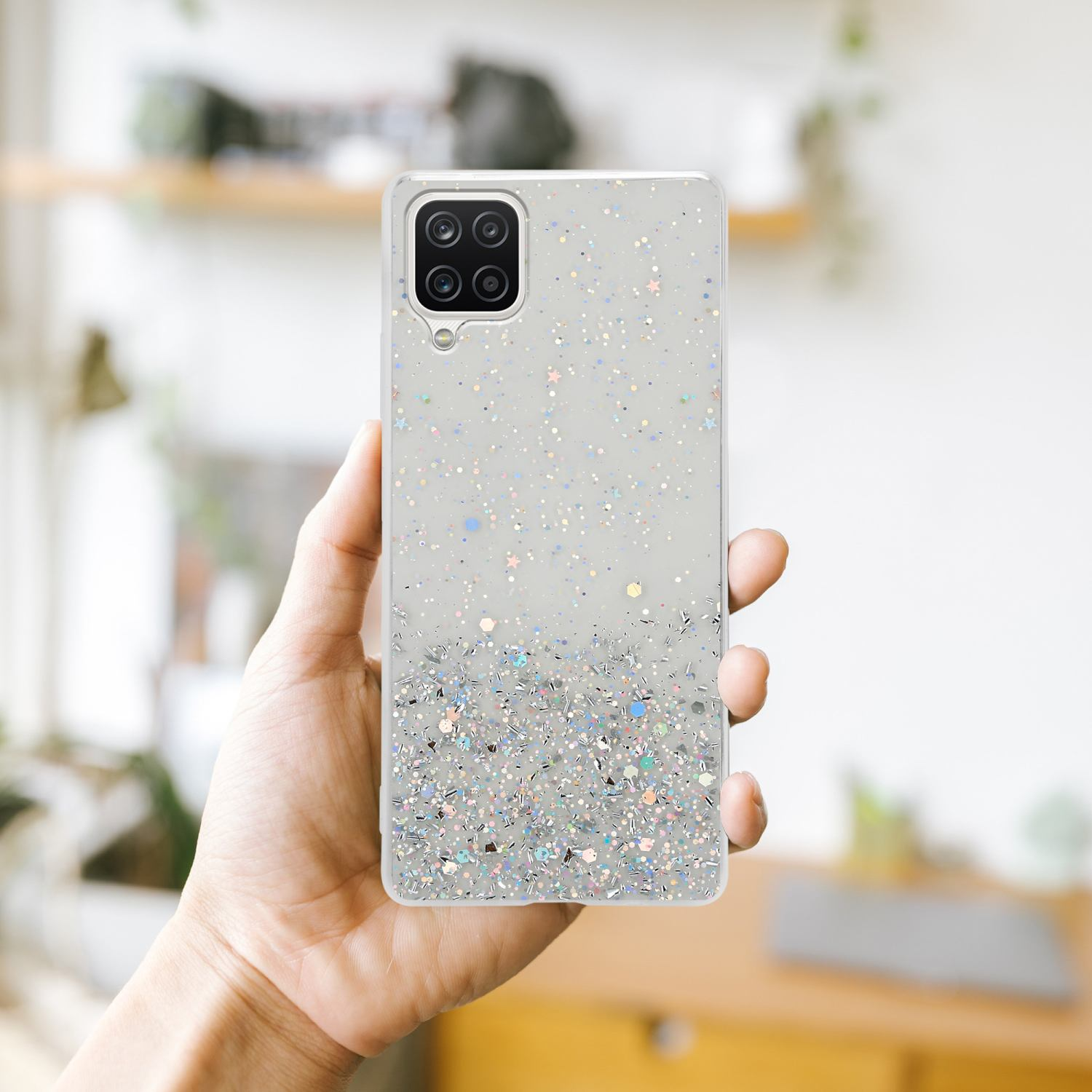 Hand hält Telefon mit Glitzerhülle. Glitzer am unteren Rand der Hülle.