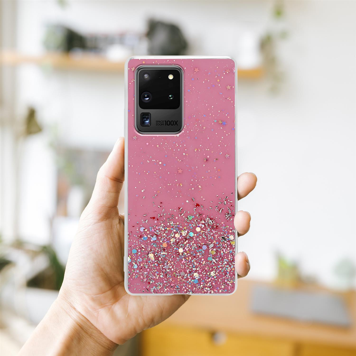 Custodia per telefono con glitter rosa in mano. Lo sfondo è un soggiorno sfocato con una finestra.