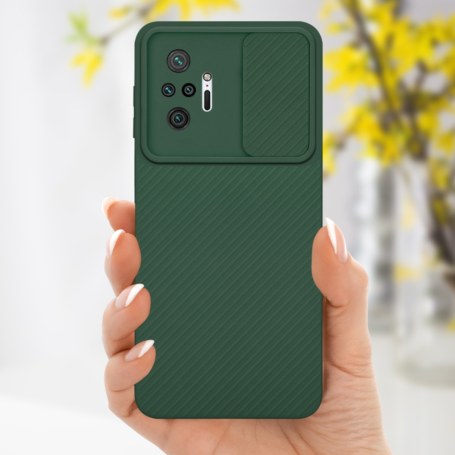 Mano che tiene una custodia verde con copertura fotocamera, con fiori sullo sfondo.