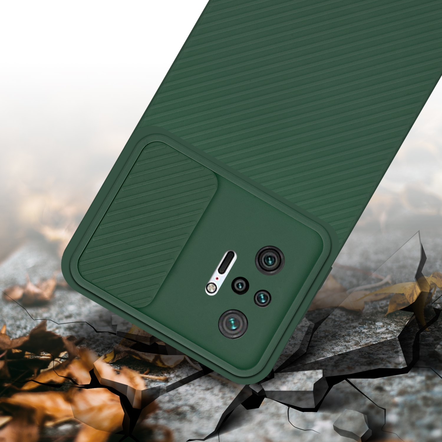 Custodia verde per telefono con copertura per fotocamera, posizionata su una superficie con crepe e foglie autunnali.