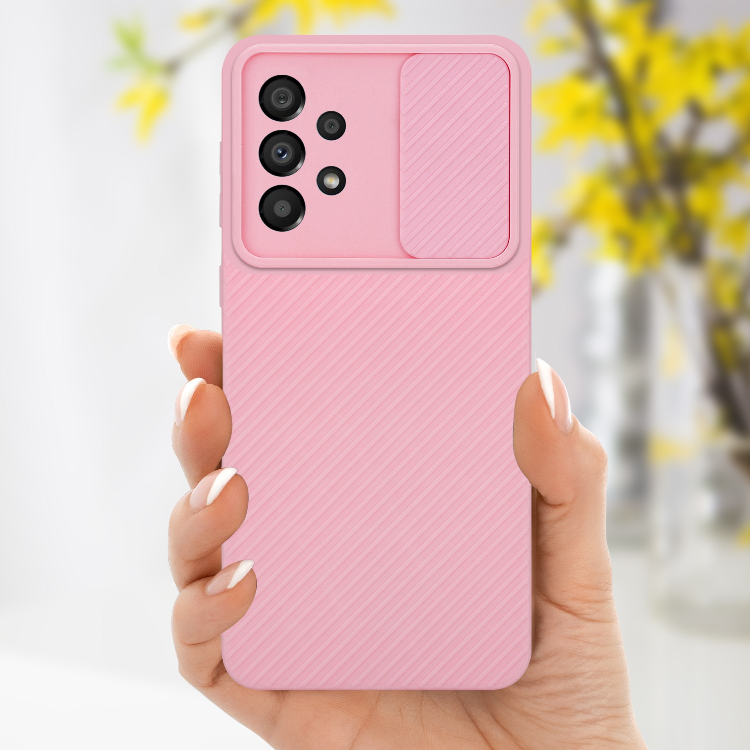 Una mano che tiene una custodia rosa con copertura della fotocamera. Fiori gialli sullo sfondo.