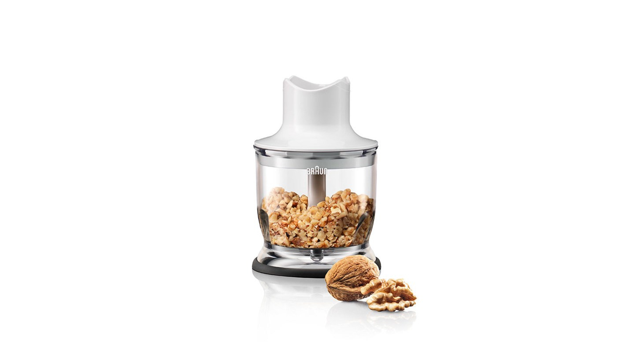 Un procesador de alimentos blanco y transparente con nueces picadas adentro y dos nueces en primer plano.