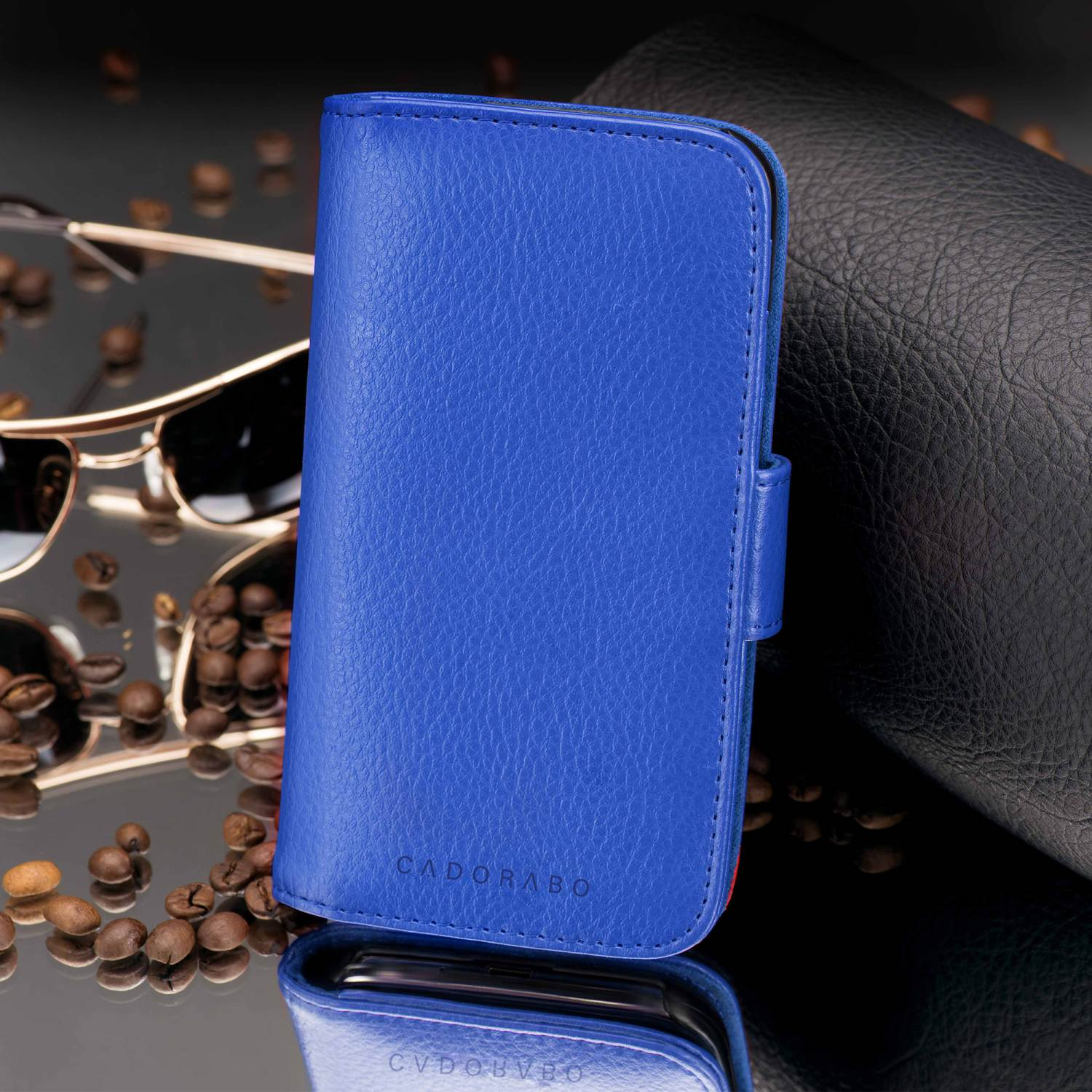 Blaue Leder-Handyhülle mit blauem Riemen. Kaffeebohnen und Sonnenbrille im Hintergrund.