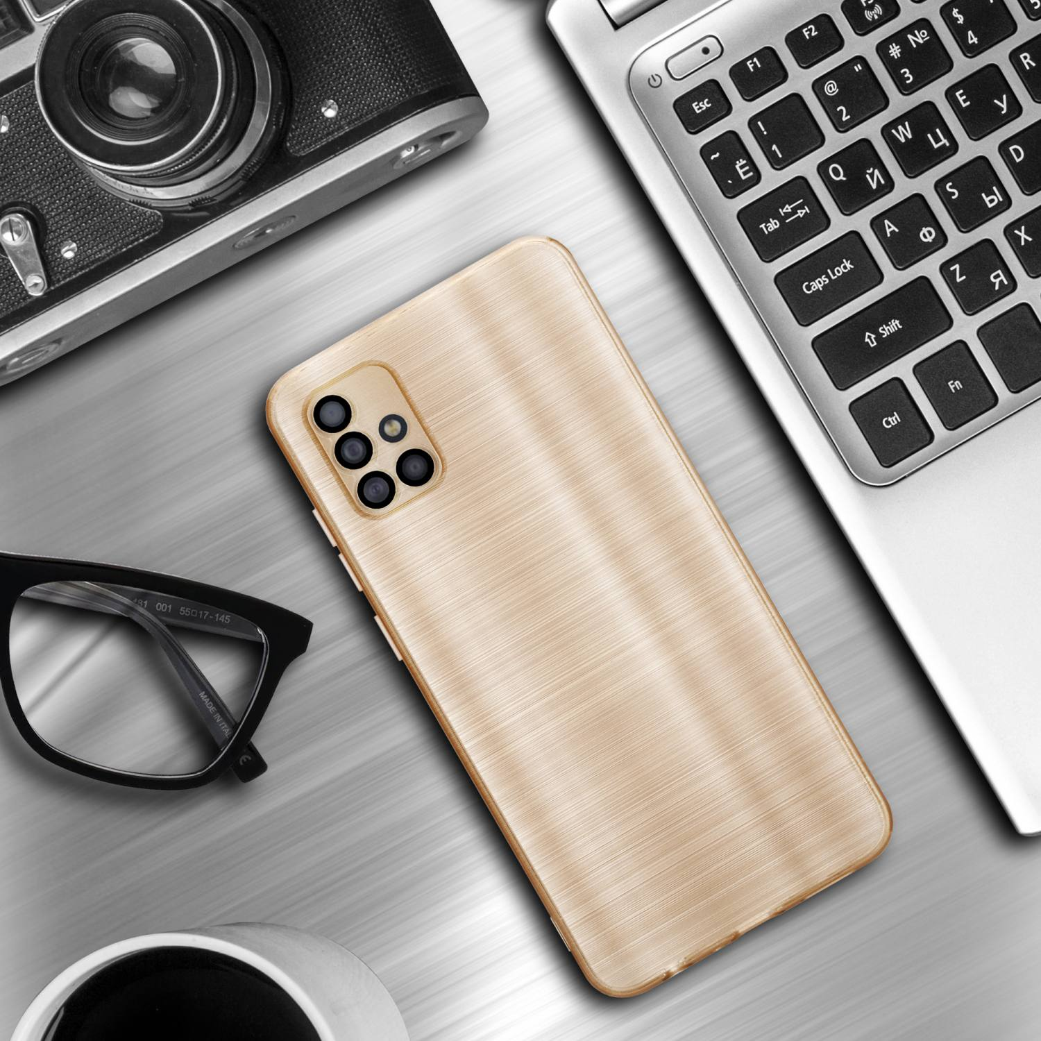 Una custodia dorata per telefono è posizionata su una superficie argentata con fotocamera, occhiali e laptop.