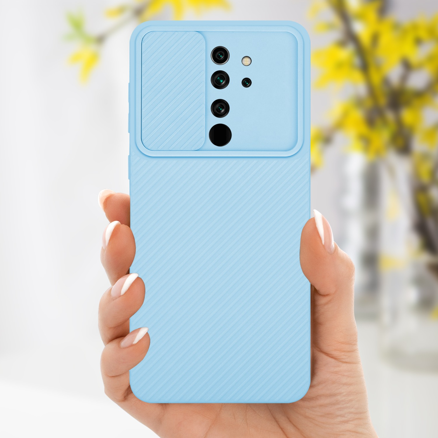 Mano che tiene una custodia per telefono azzurra con copertura per fotocamera. Fiori gialli sullo sfondo.