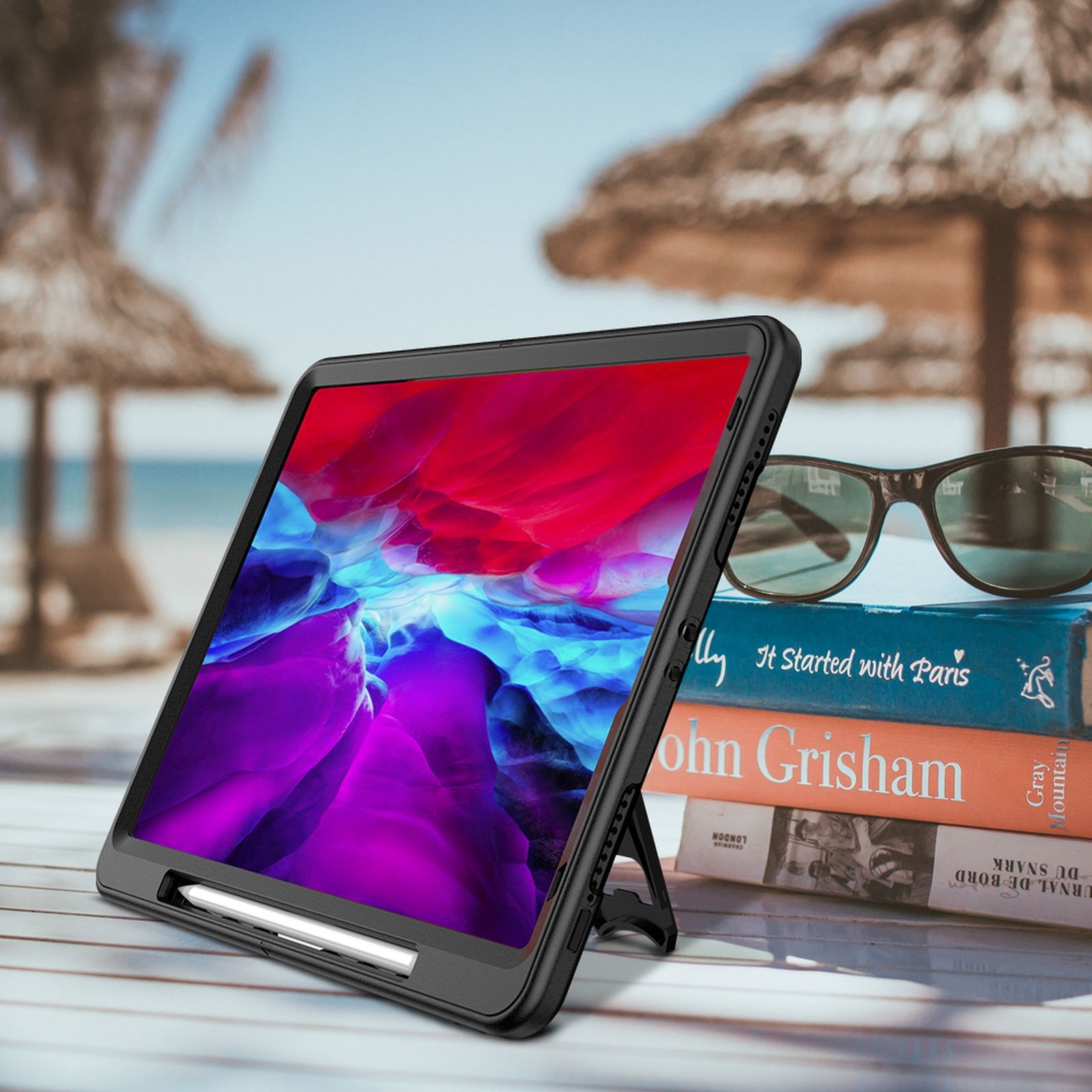 Tablet in schwarzer Hülle, auf einem Tisch mit Büchern und Sonnenbrille.