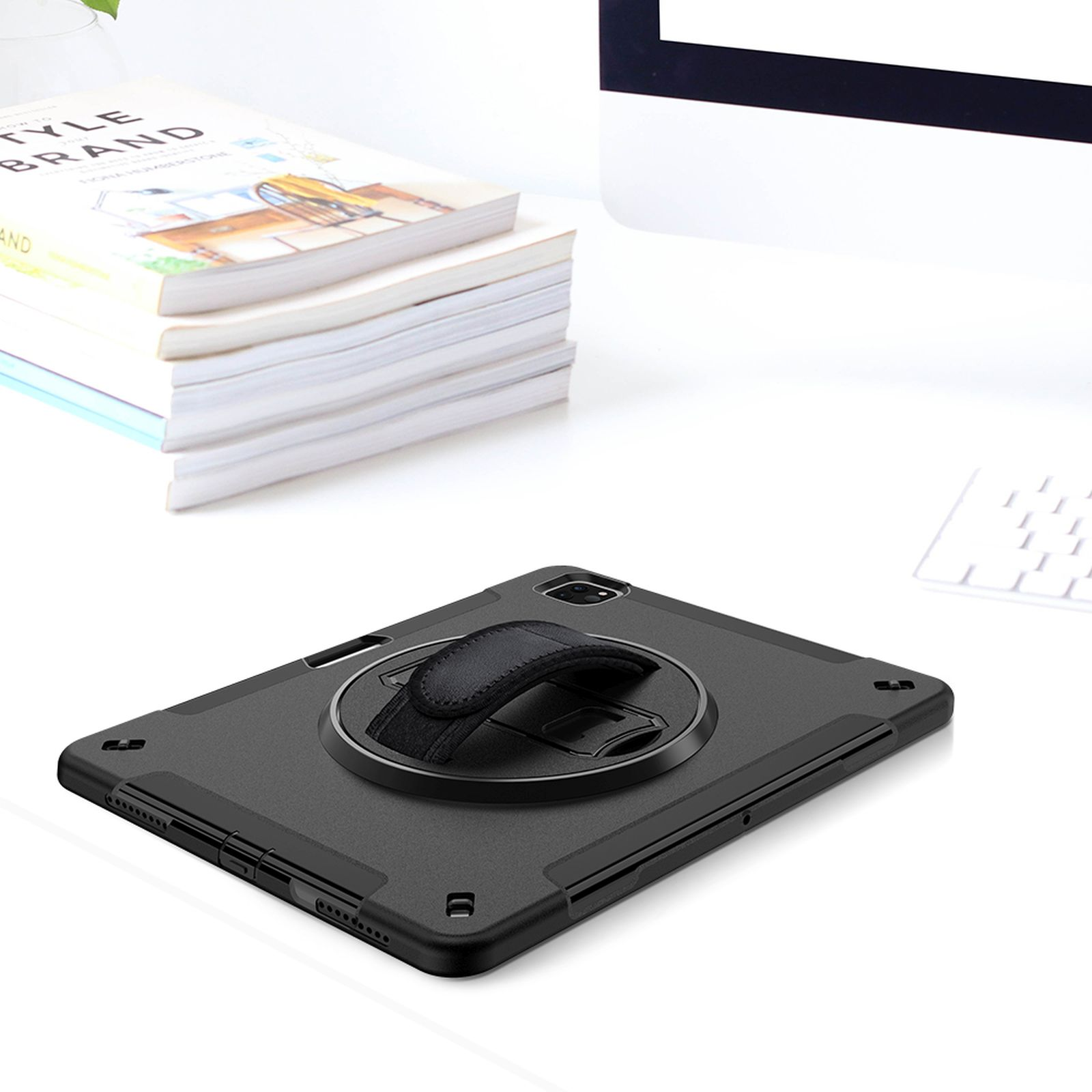 Ein schwarzes Tablet mit Handschlaufe und Drehscheibe. Das Tablet liegt auf einem weißen Schreibtisch mit Büchern und Monitor.