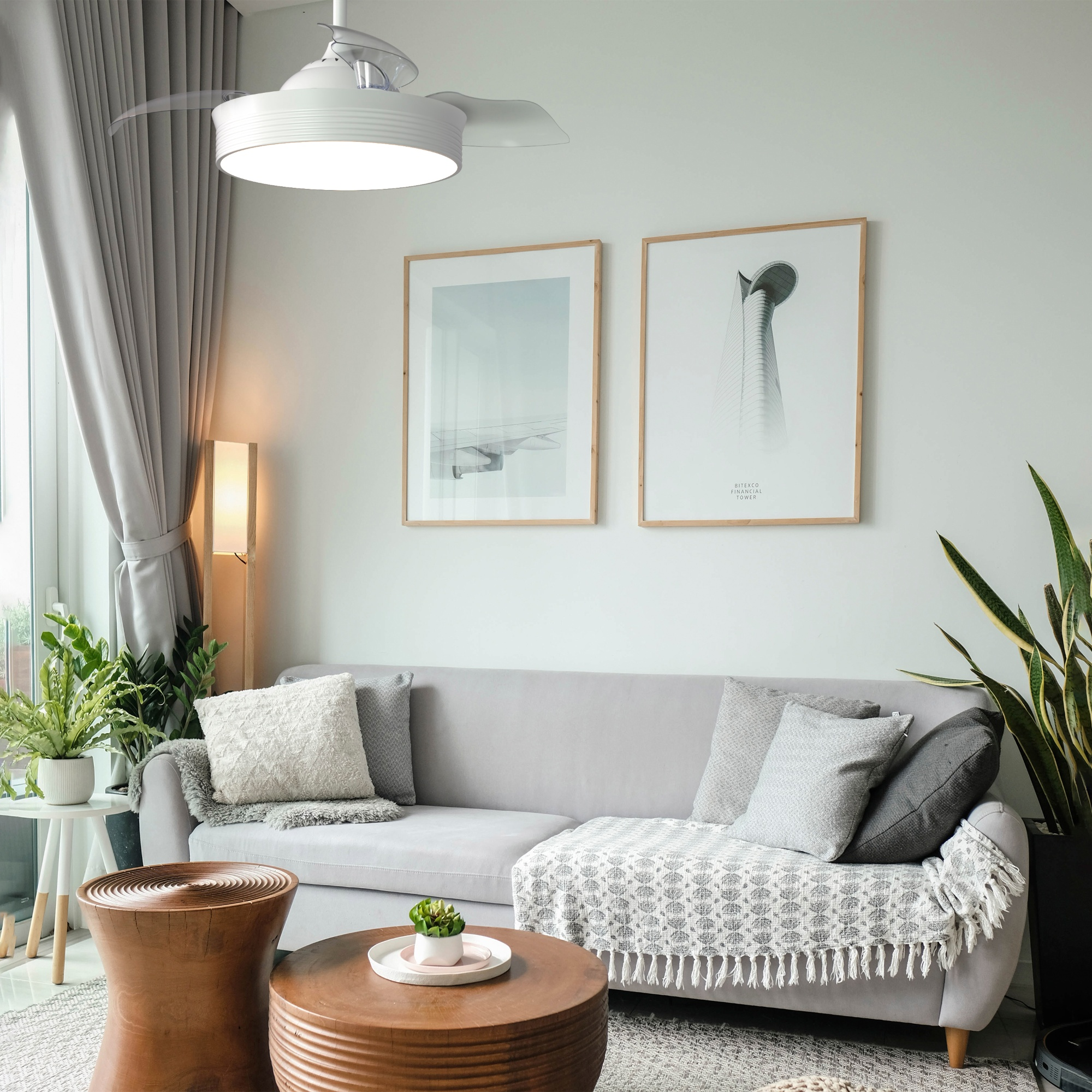 Escena de sala de estar con sofá, arte, plantas y ventilador de techo. Paredes gris claro y detalles en madera. Acogedor.
