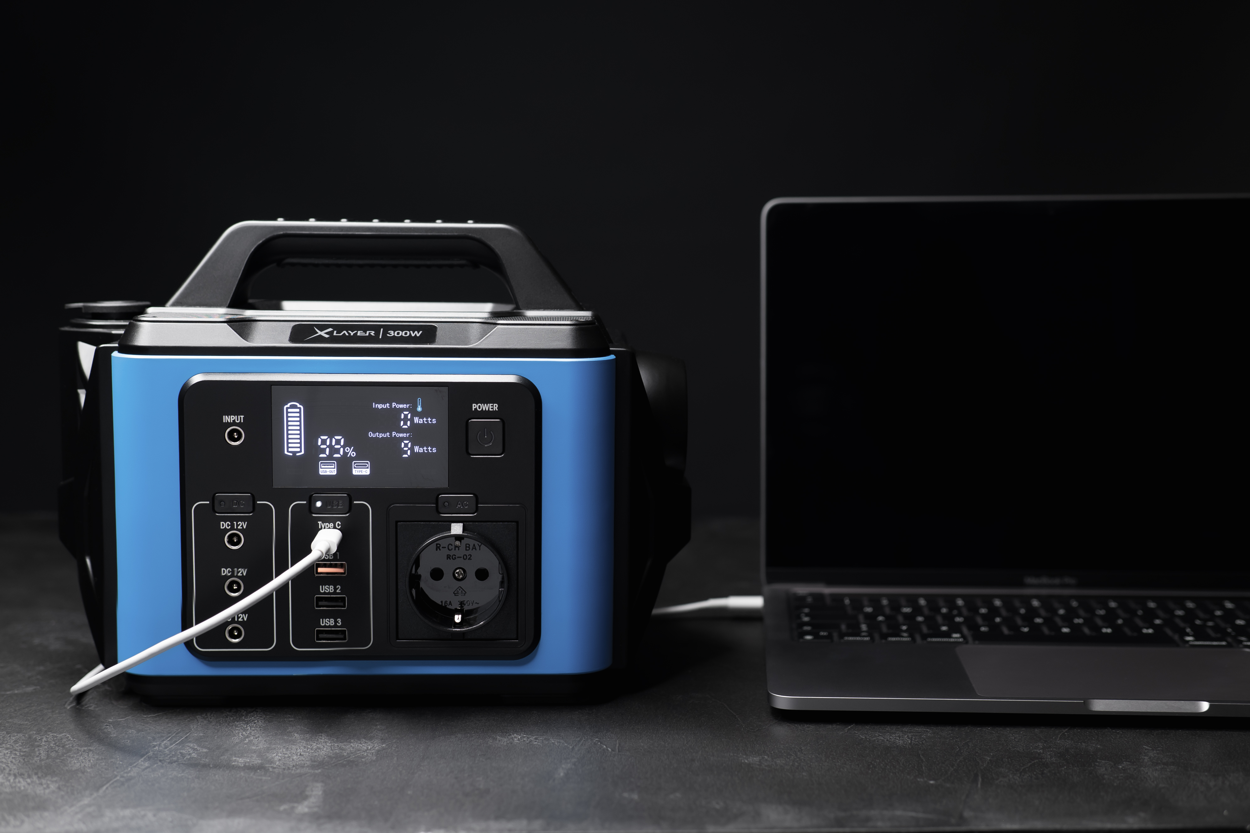 Centrale elettrica blu che carica un laptop. Display con 99%. Sfondo nero.