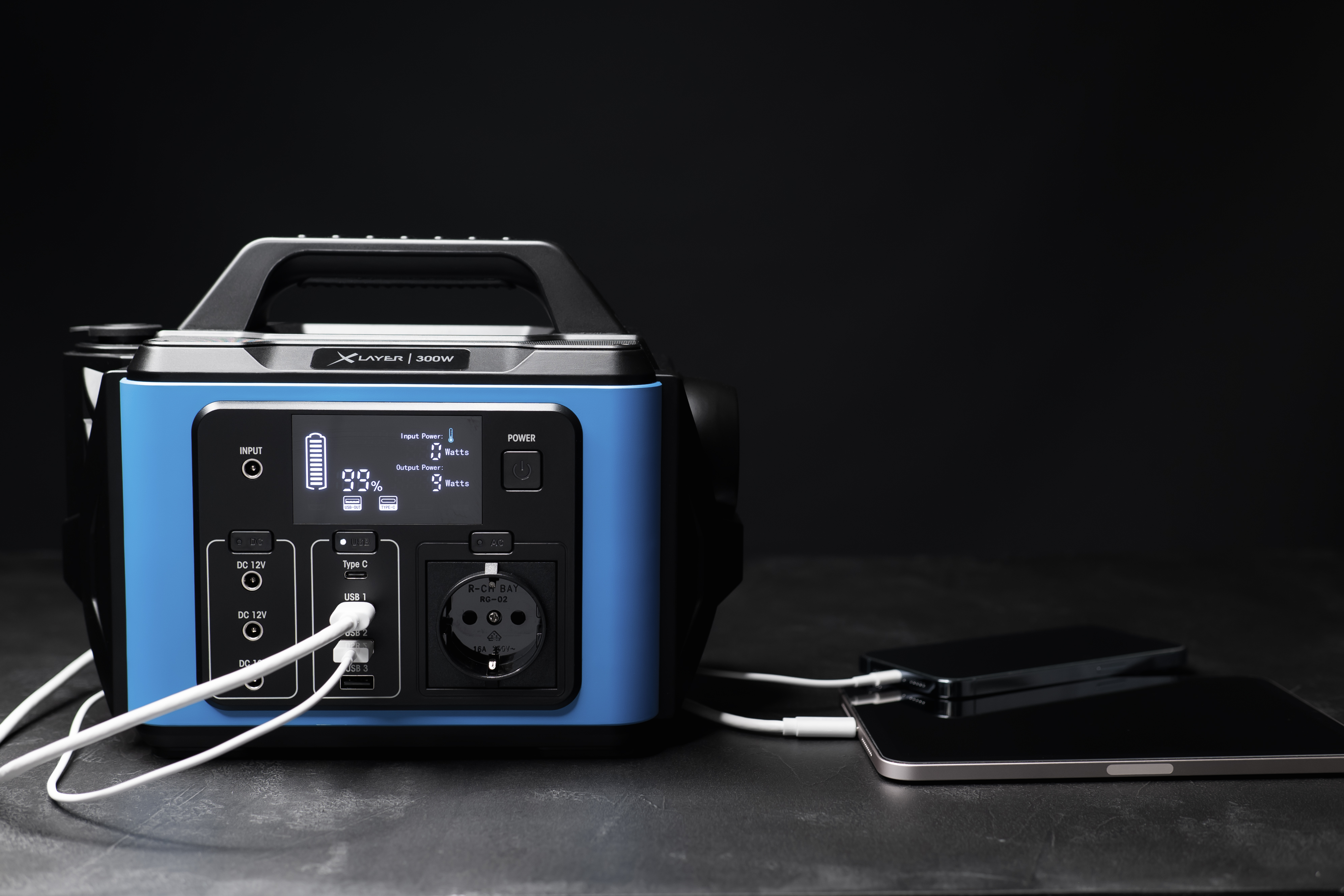 Centrale elettrica blu con dispositivi collegati, carica tablet e telefono. Sfondo nero.