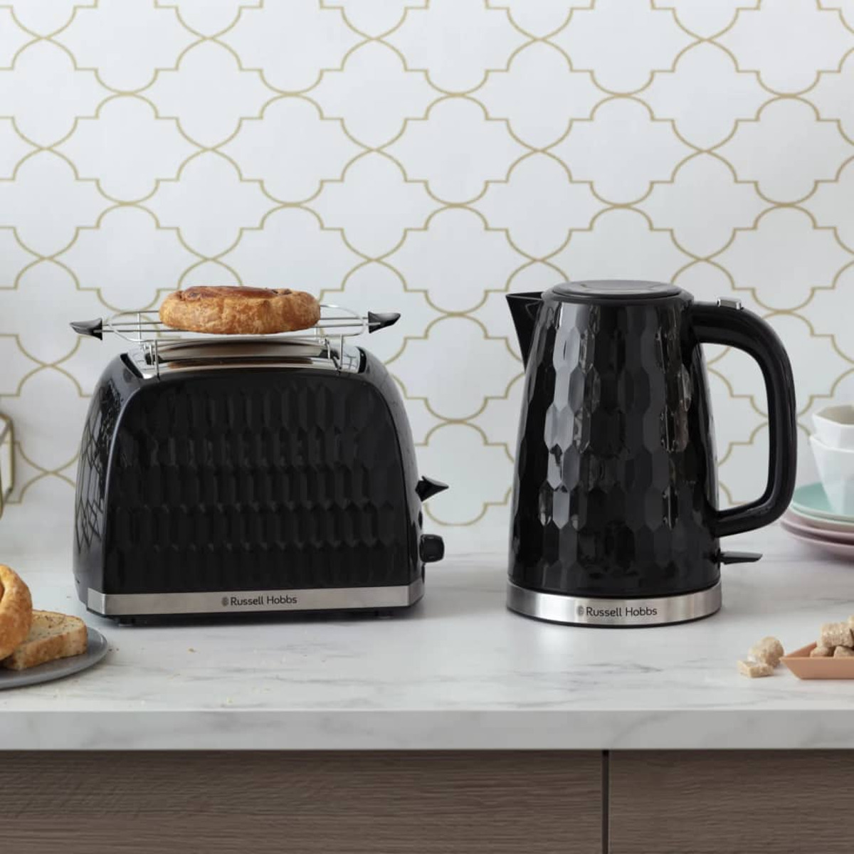 Schwarzes Toaster- und Wasserkocher-Set auf Marmorplatte. Gebäck im Toaster.