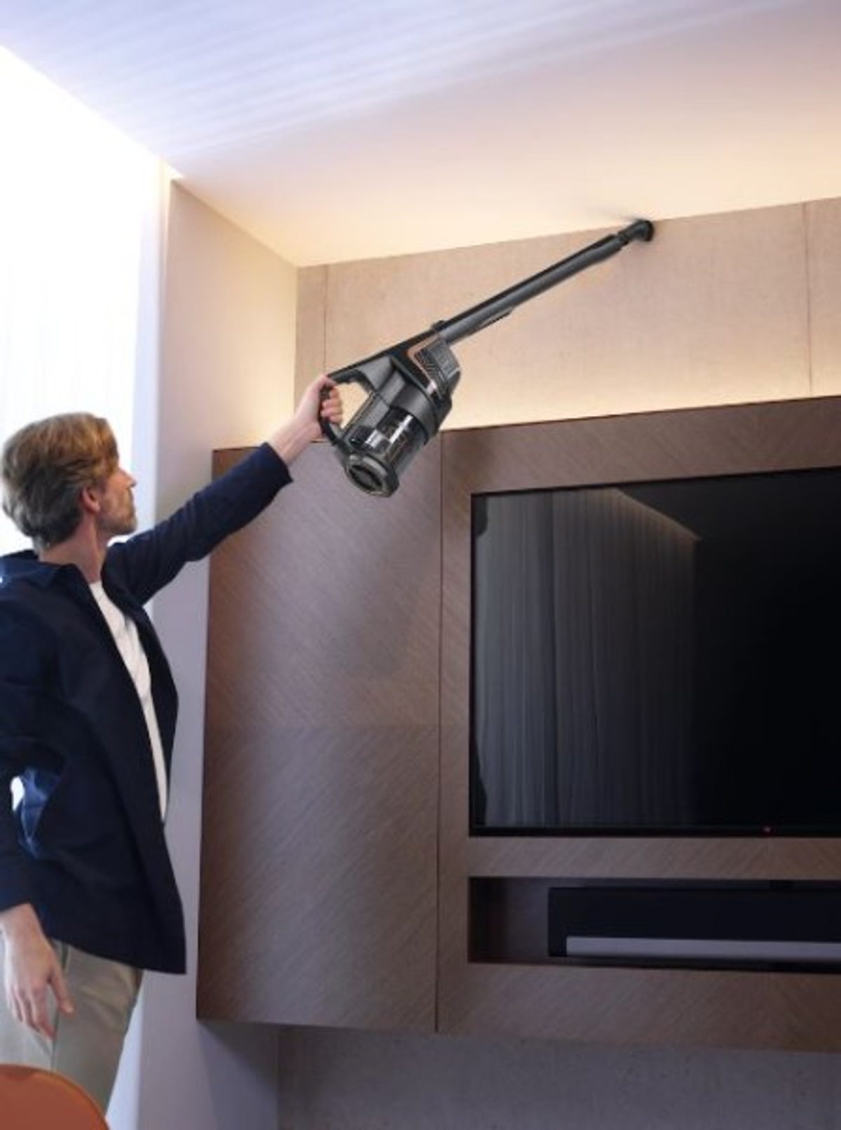 Un uomo che aspira un muro con un aspirapolvere portatile vicino a un televisore e un pannello di legno.