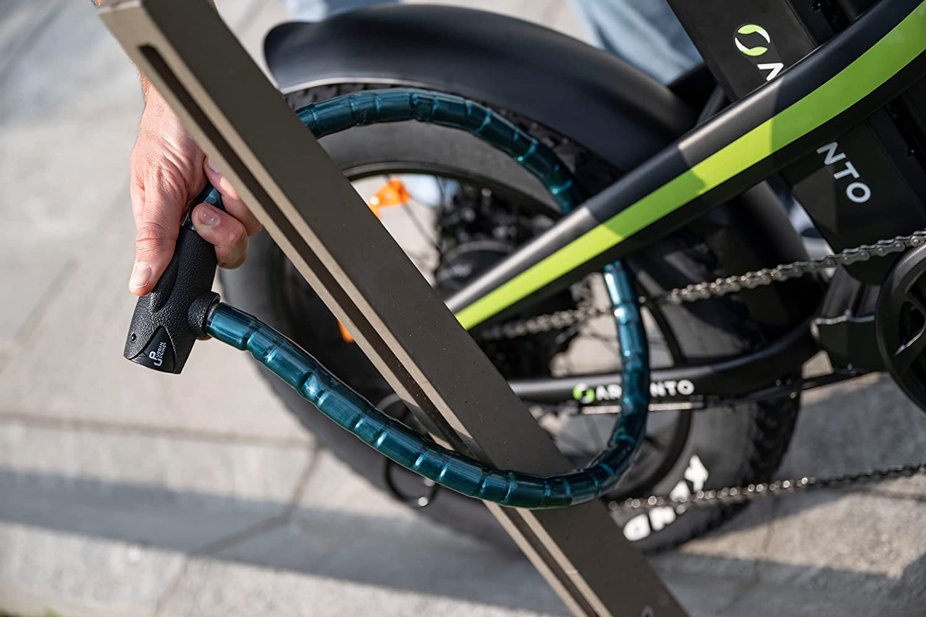 Una mano cerrando una cerradura de bicicleta azul en una bicicleta eléctrica negra y verde, al aire libre.