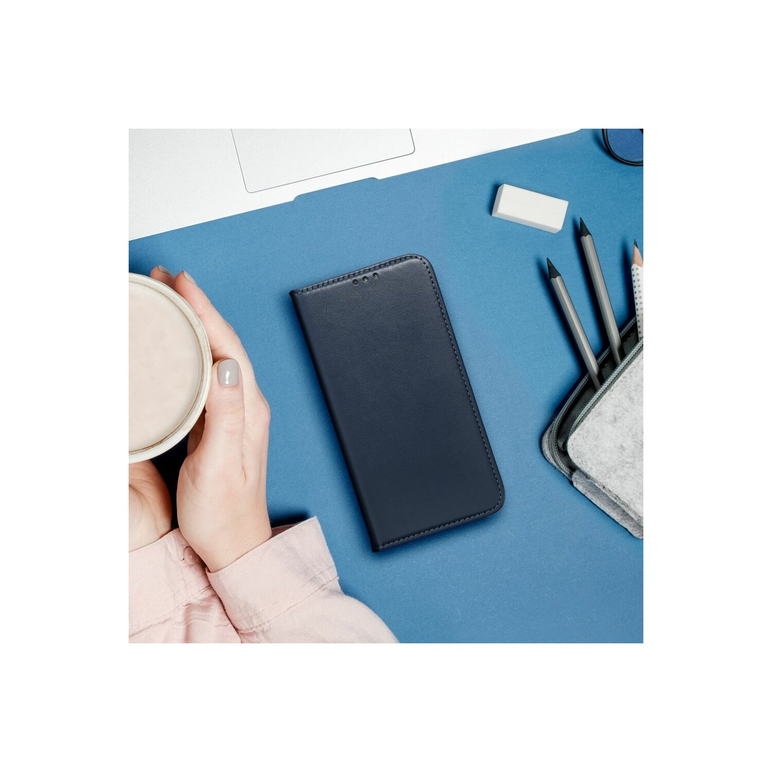 Eine Hand hält eine Handyhülle, mit Laptop, Bleistiften und einer Tasse auf dem Tisch.
