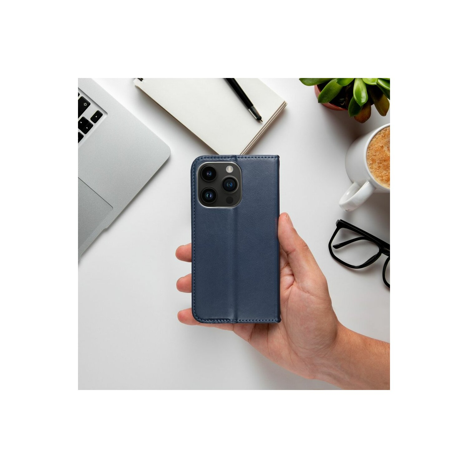 Hand, die eine blaue Handyhülle hält, neben Laptop, Kaffee und Brille.