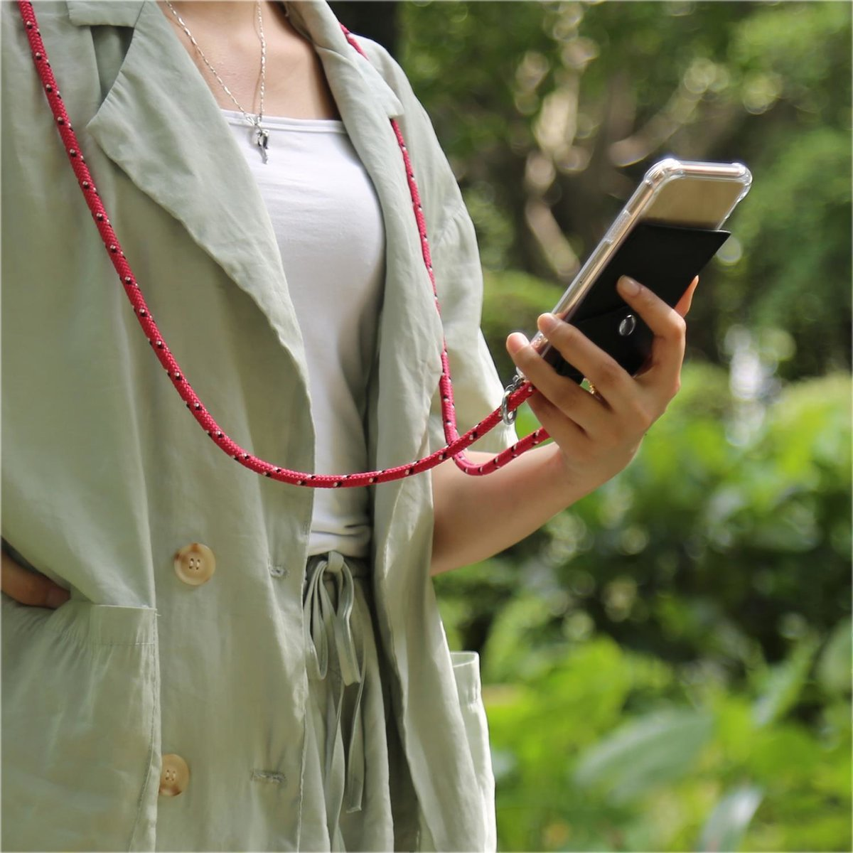 Una persona tiene in mano un telefono in una custodia nera con un cordino rosso e bianco.