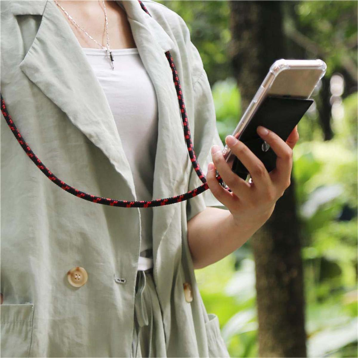 Donna che tiene in mano un telefono in una custodia attaccata a un cordino rosso e nero, all'aperto in un parco.