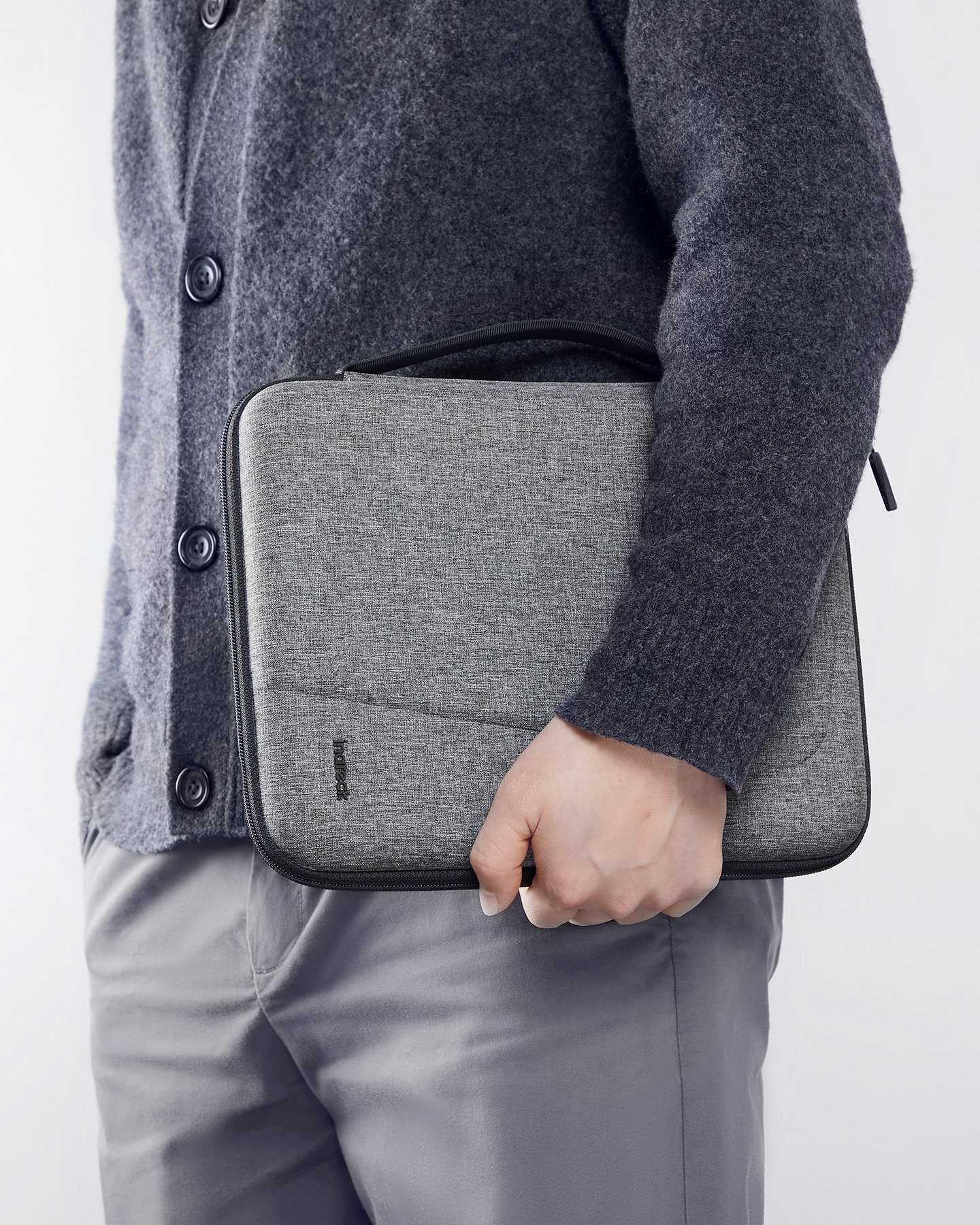 Eine Person hält einen grauen Laptop-Koffer mit schwarzem Griff und sichtbarer Naht.