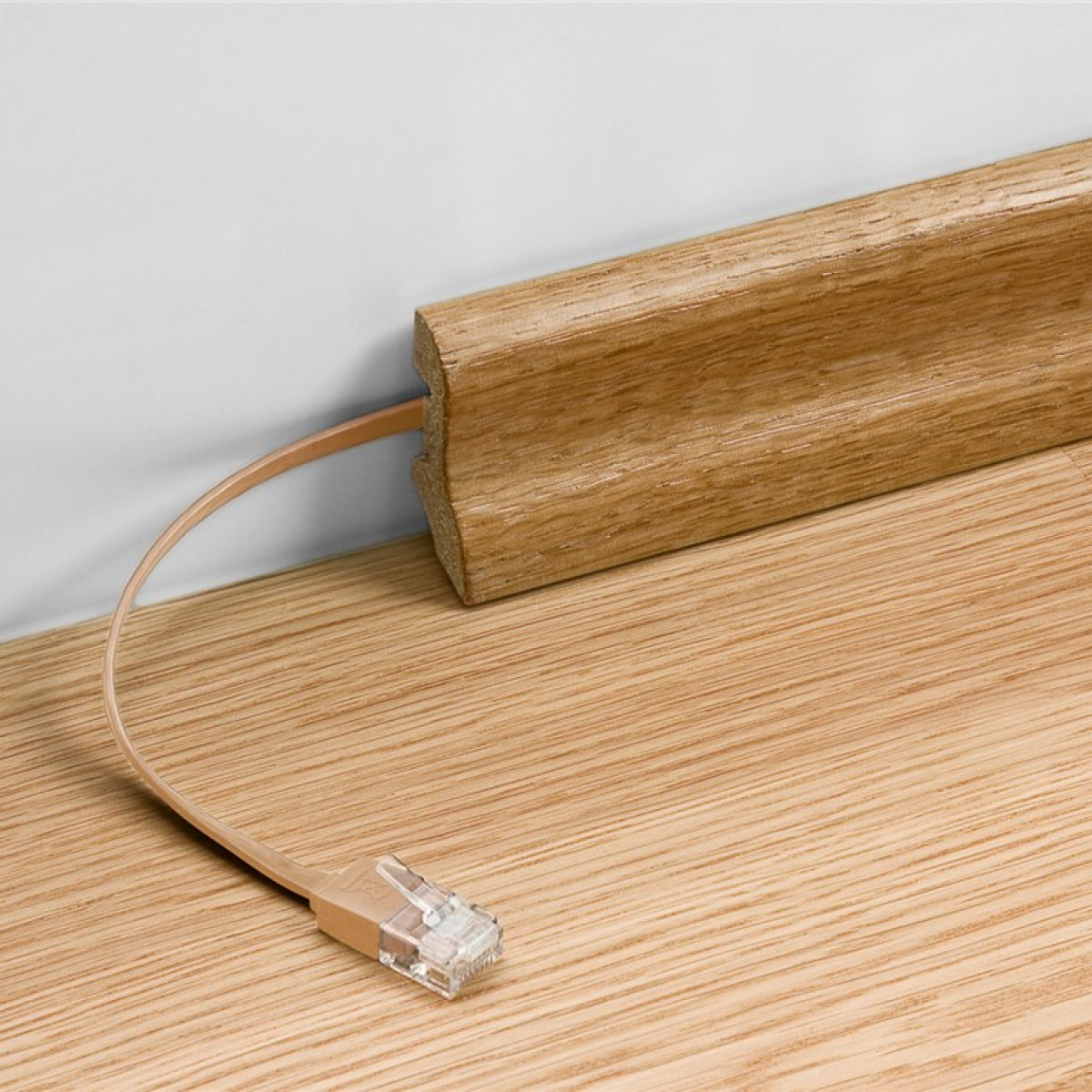 Ein Netzwerkkabel ist mit einer Holzfußleiste verbunden. Das Kabel ist beige.